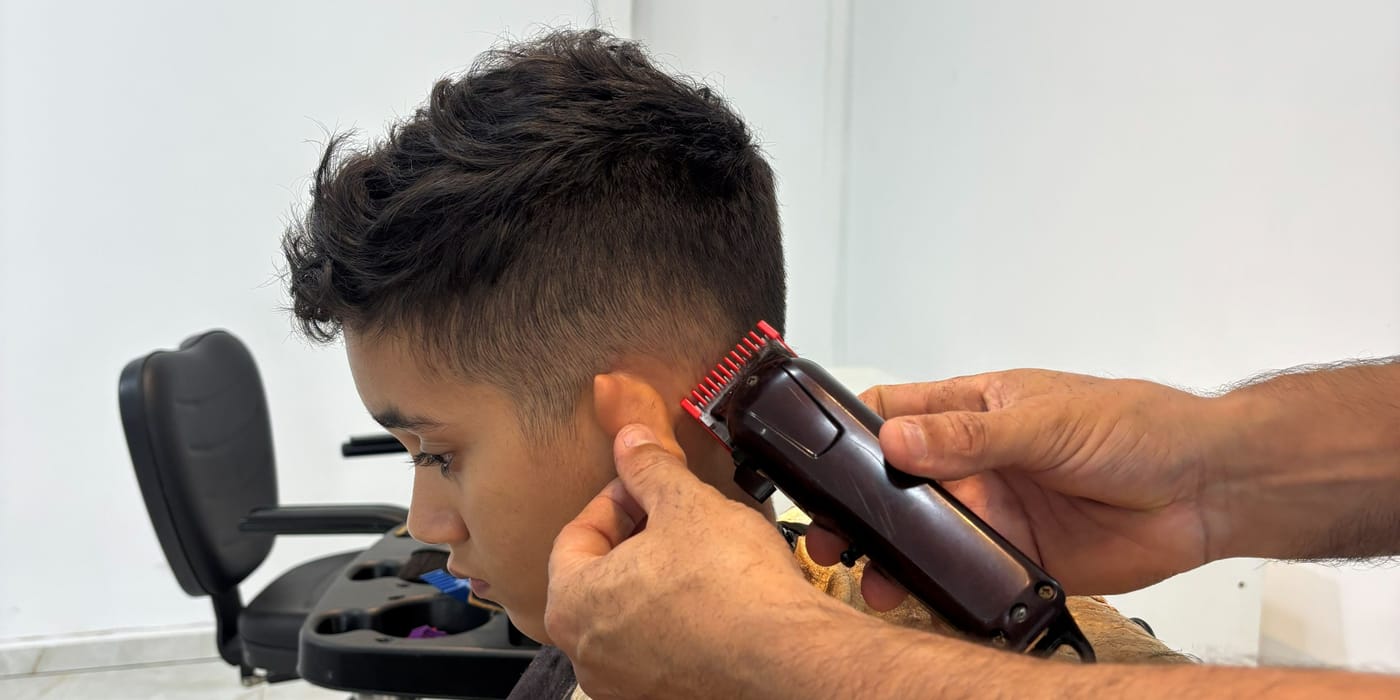 Barbeiro finalizando um corte com máquina e acabamento atrás da orelha, na barbearia do salão