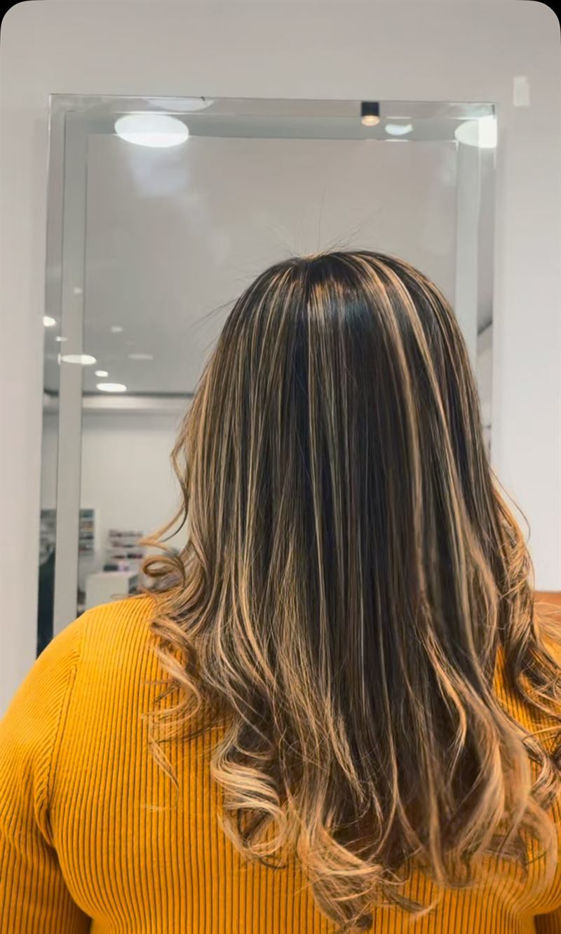 Cabelo escuro com mechas claras e pontas onduladas, de costas